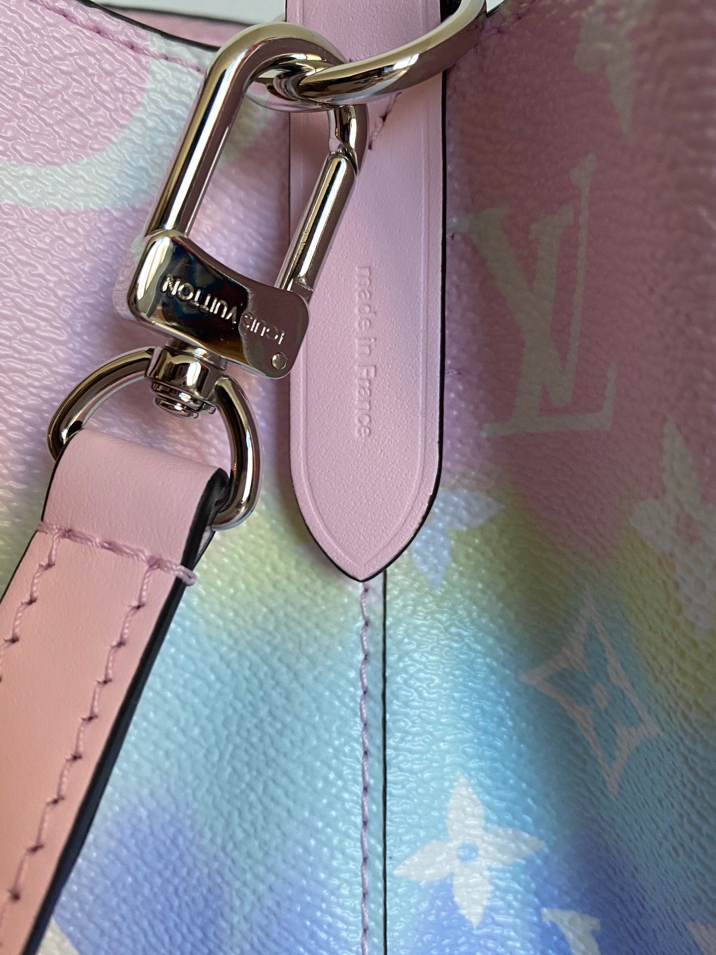 Close-up of a pink handbag strap with gold hardware on a multicolored patterned background.
