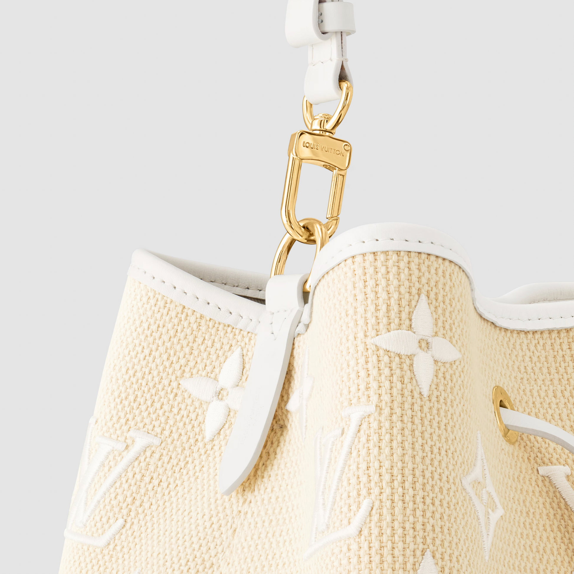 Close-up of a beige handbag with white floral patterns and gold hardware on a light gray background
