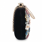 Black velvet clutch with floral embellishments and a chain strap on a white background
