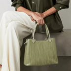 Person holding a green handbag with a neutral background