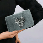 Gray clutch with decorative embellishments held by a person against a neutral background