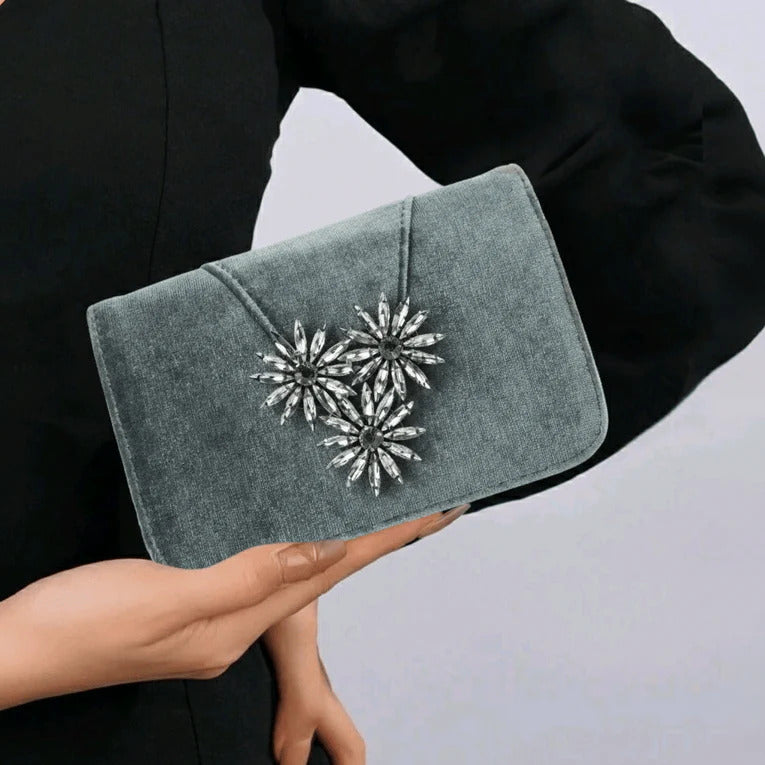 Gray clutch with decorative embellishments held by a person against a neutral background