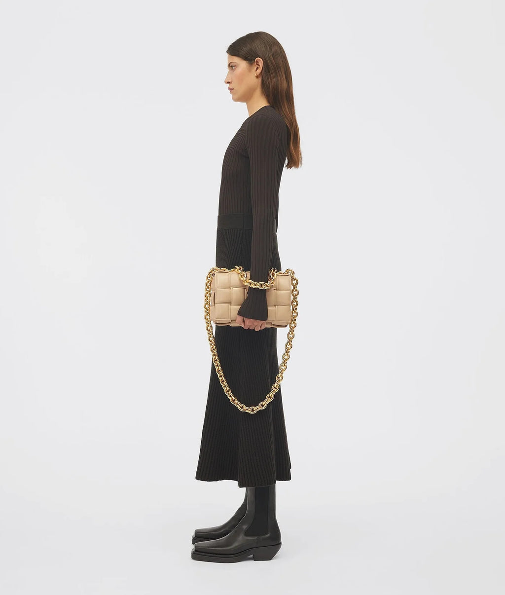 Woman holding a beige handbag with gold chain strap on a white background