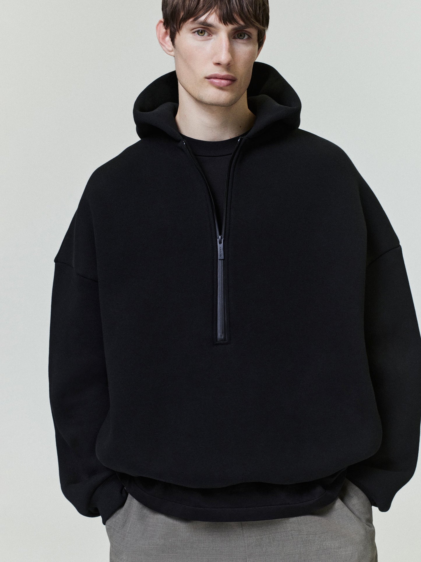 Man wearing a black hoodie with a zipper on a plain background