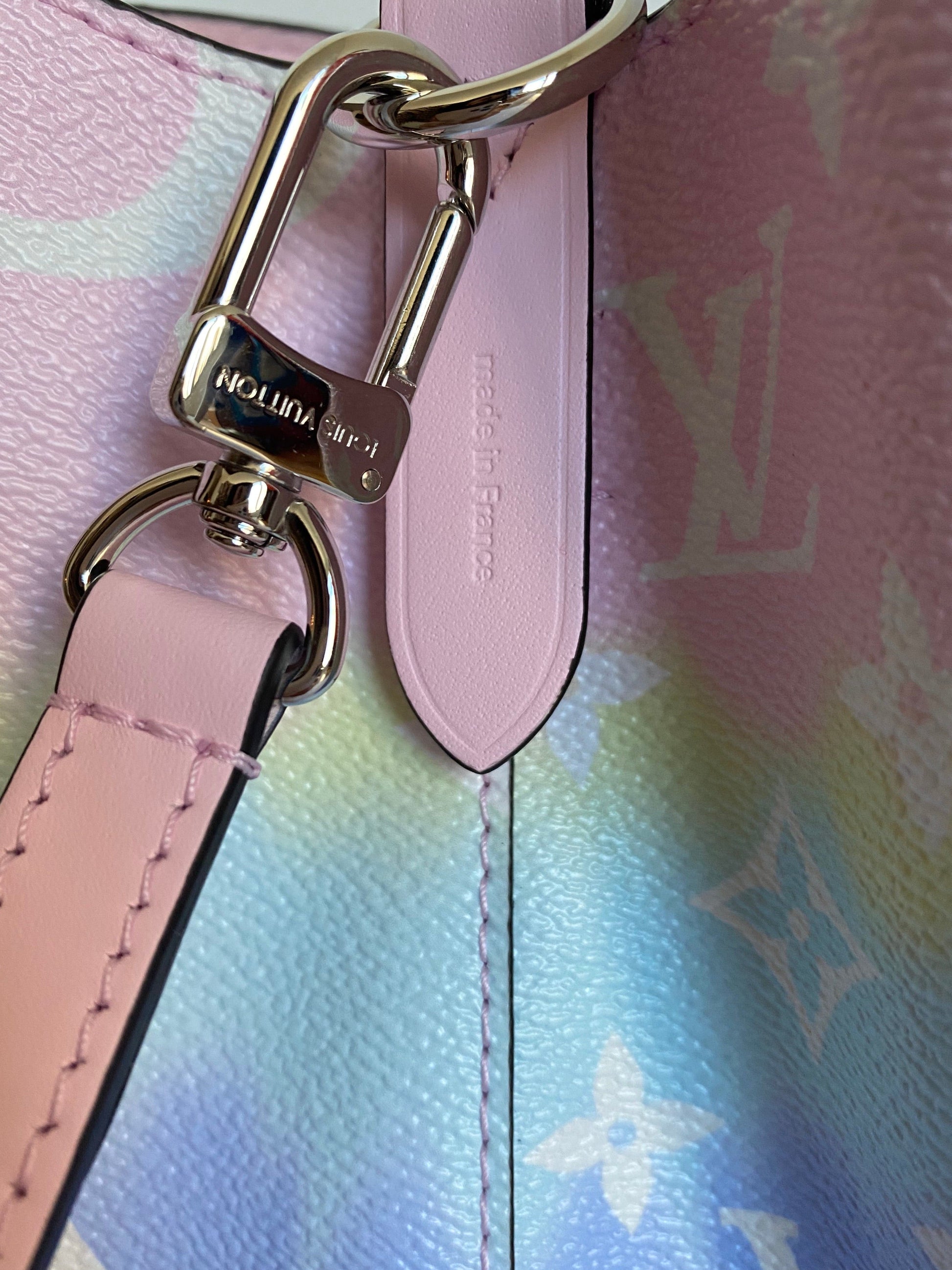 Close-up of a pink handbag strap with gold hardware on a multicolored patterned background.