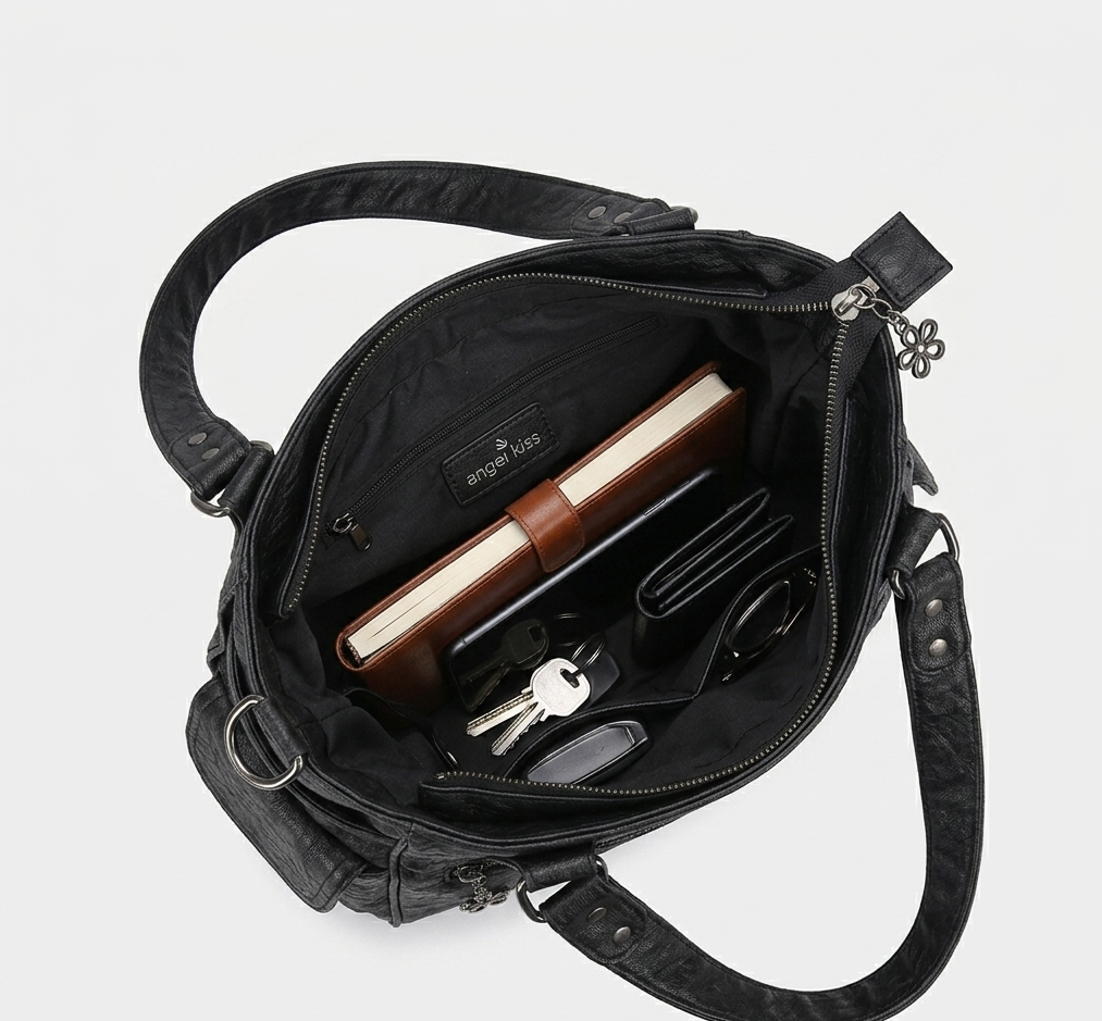 Black leather bag with compartments containing a notebook, pen, and other items on a white background