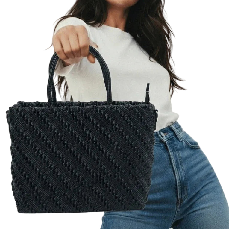 Person holding a black woven handbag against a neutral background