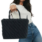 Person holding a black woven handbag against a neutral background